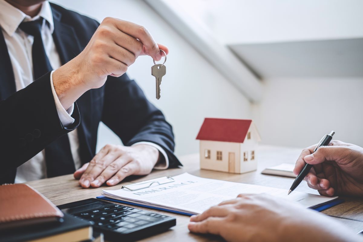 An agent hands a set of house keys to someone signing insurance papework.