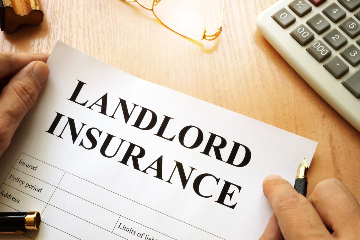A paper on a desk surrounded by a calculator, glasses, and a pen, reads "Landlord Insurance"