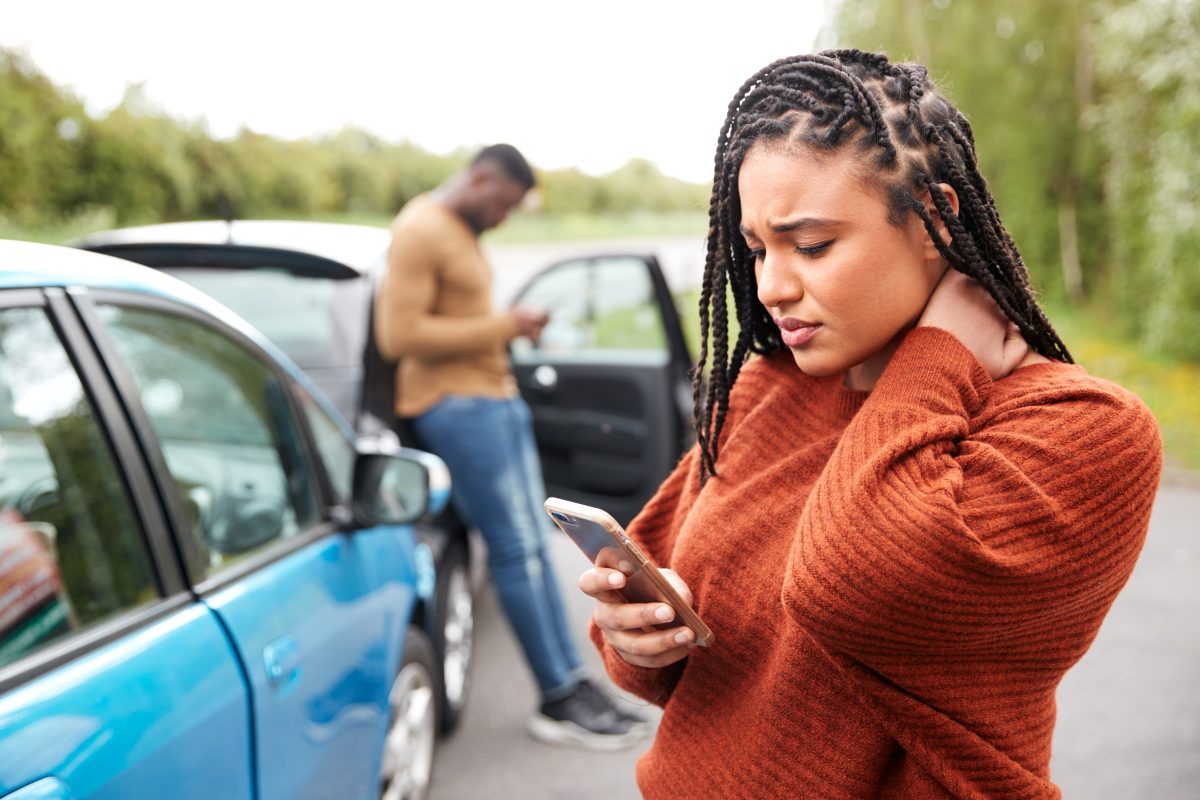 A woman with braids checks her phone after getting into a car accident.